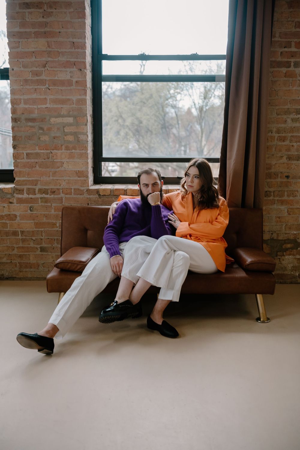 A couple relaxes together in a sunlit room with exposed brick walls and windows.