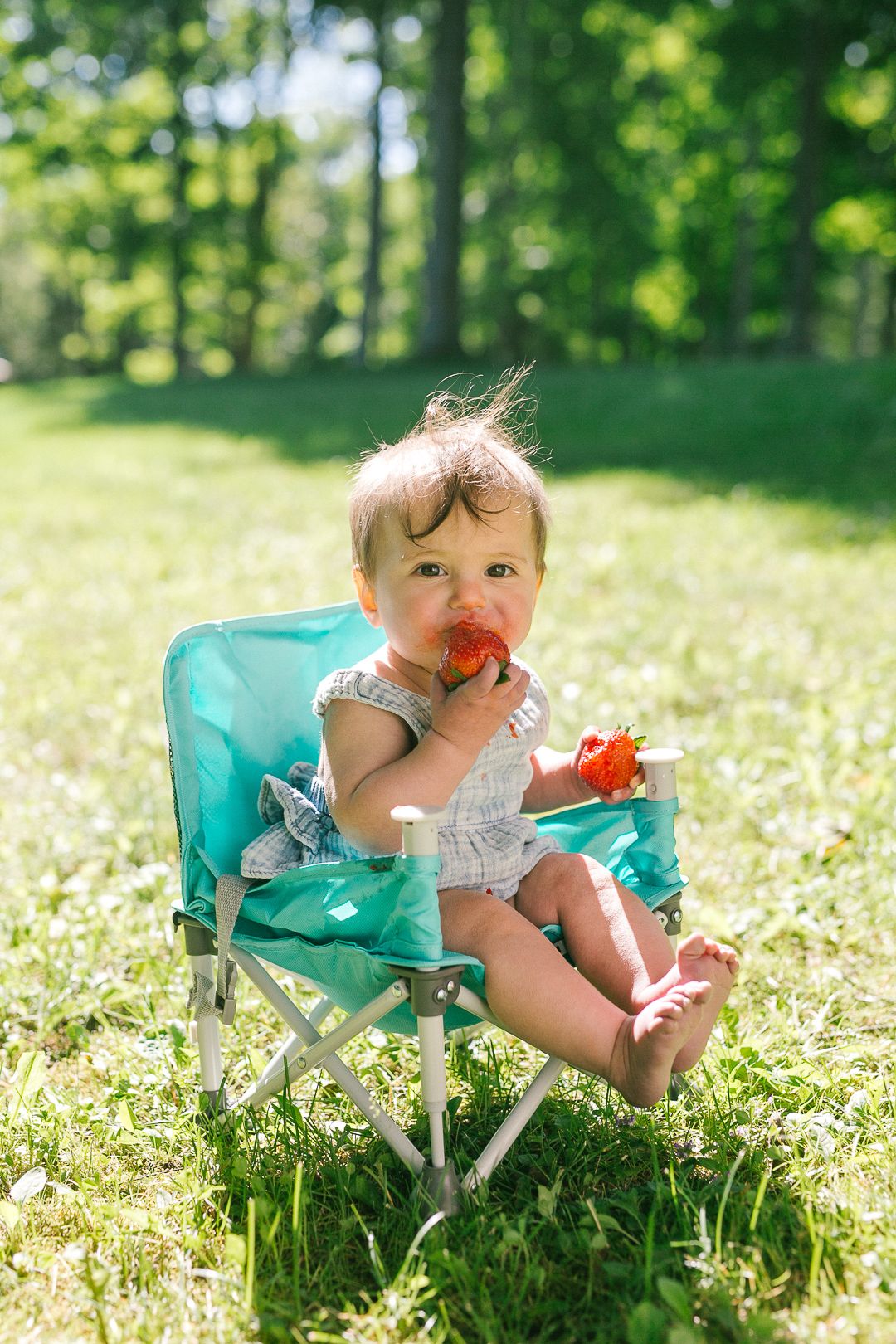A small child sits in a turquoise chair among blooming wildflowers in a sunny meadow on a summer day.