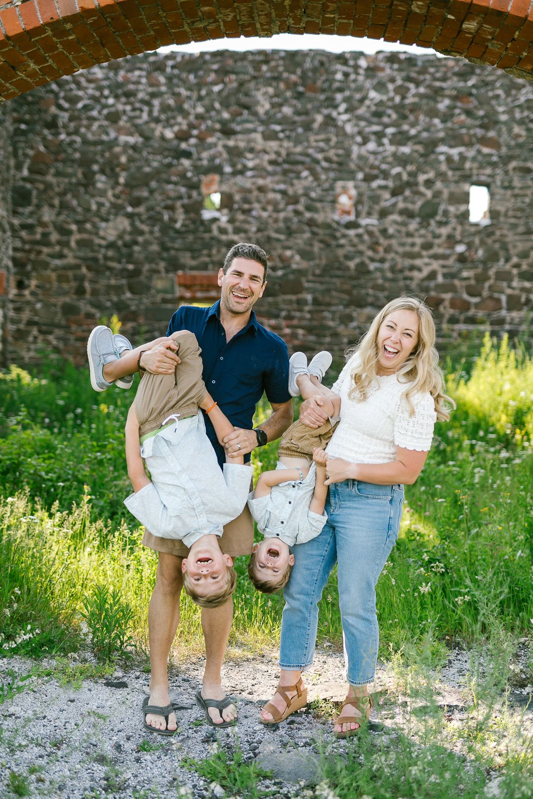 Playful family moment captured in a series of photos against a stone wall and grassy field.