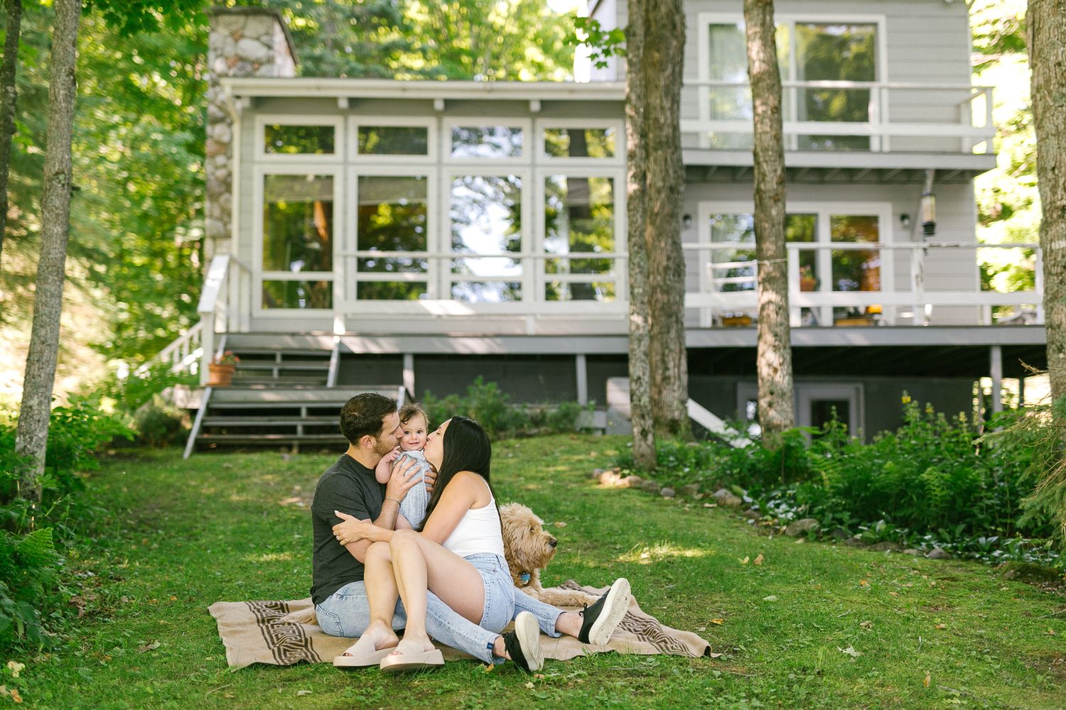 A couple relaxes on outdoor lounge chairs while using laptops in a peaceful backyard garden setting.