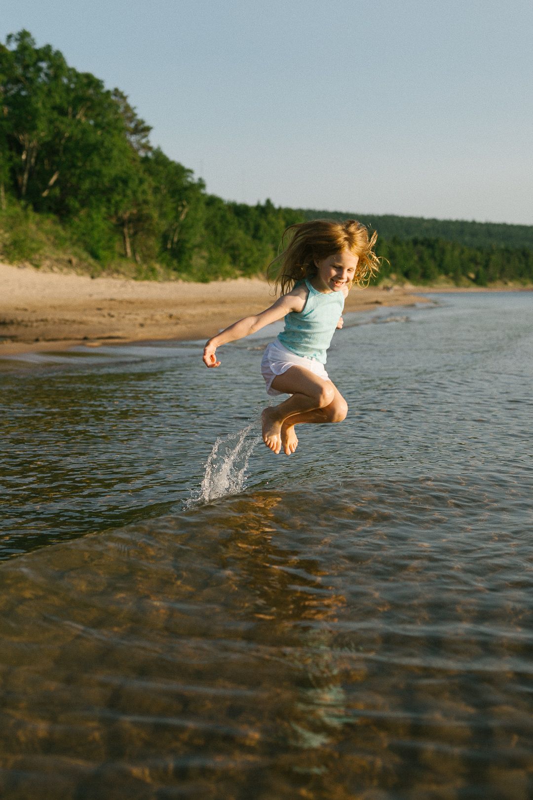 A person splashing and playing in shallow water at the beach during sunset.