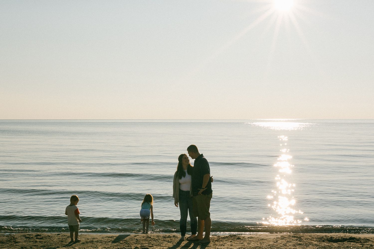 Silhouettes of people walking along a scenic beach at sunset with golden light reflecting on the ocean.