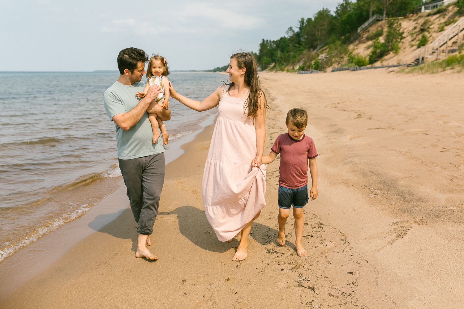 A family walks together along a sandy beach shoreline on a sunny summer day.