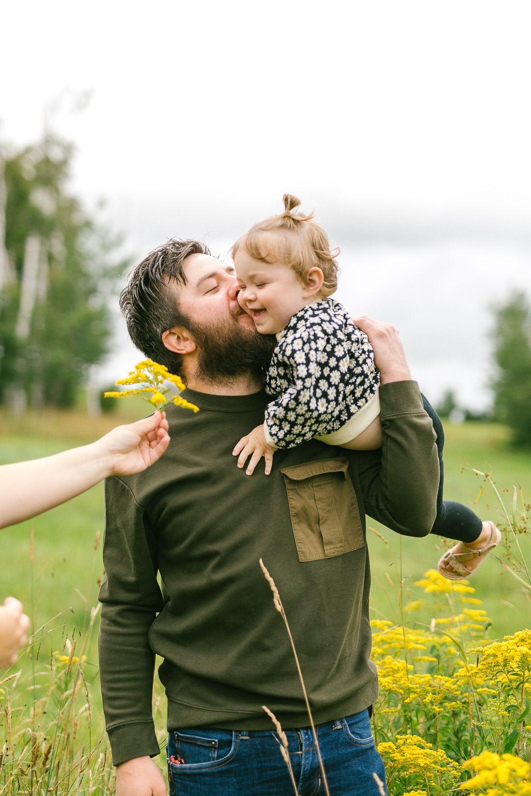 Family playing together in a field of yellow wildflowers on a sunny day.