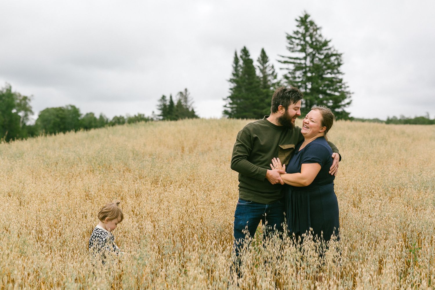 Candid family moment captured in a golden wheat field during sunset.