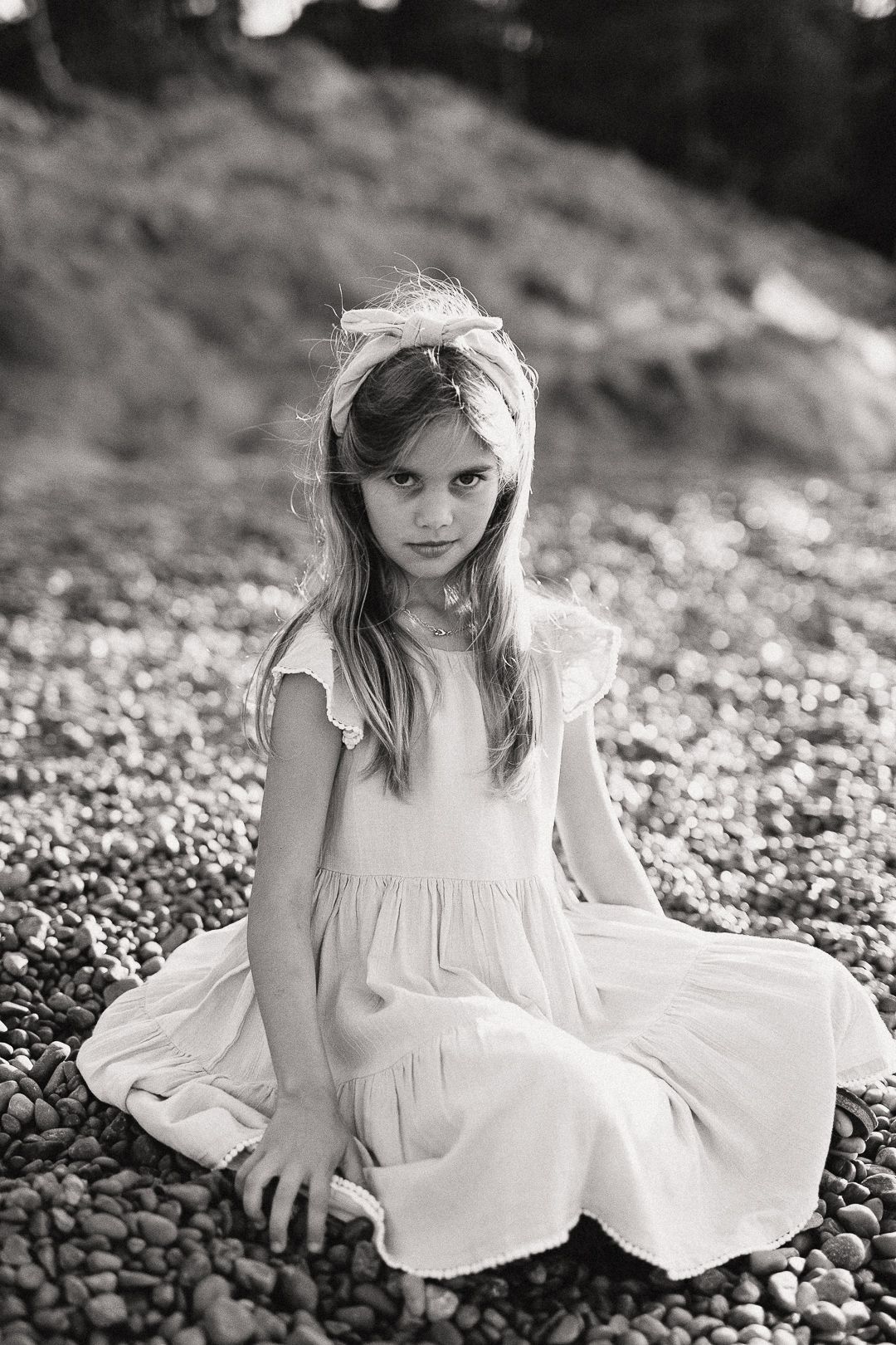 Black and white portrait series showing figure in white dress sitting on rocky ground.