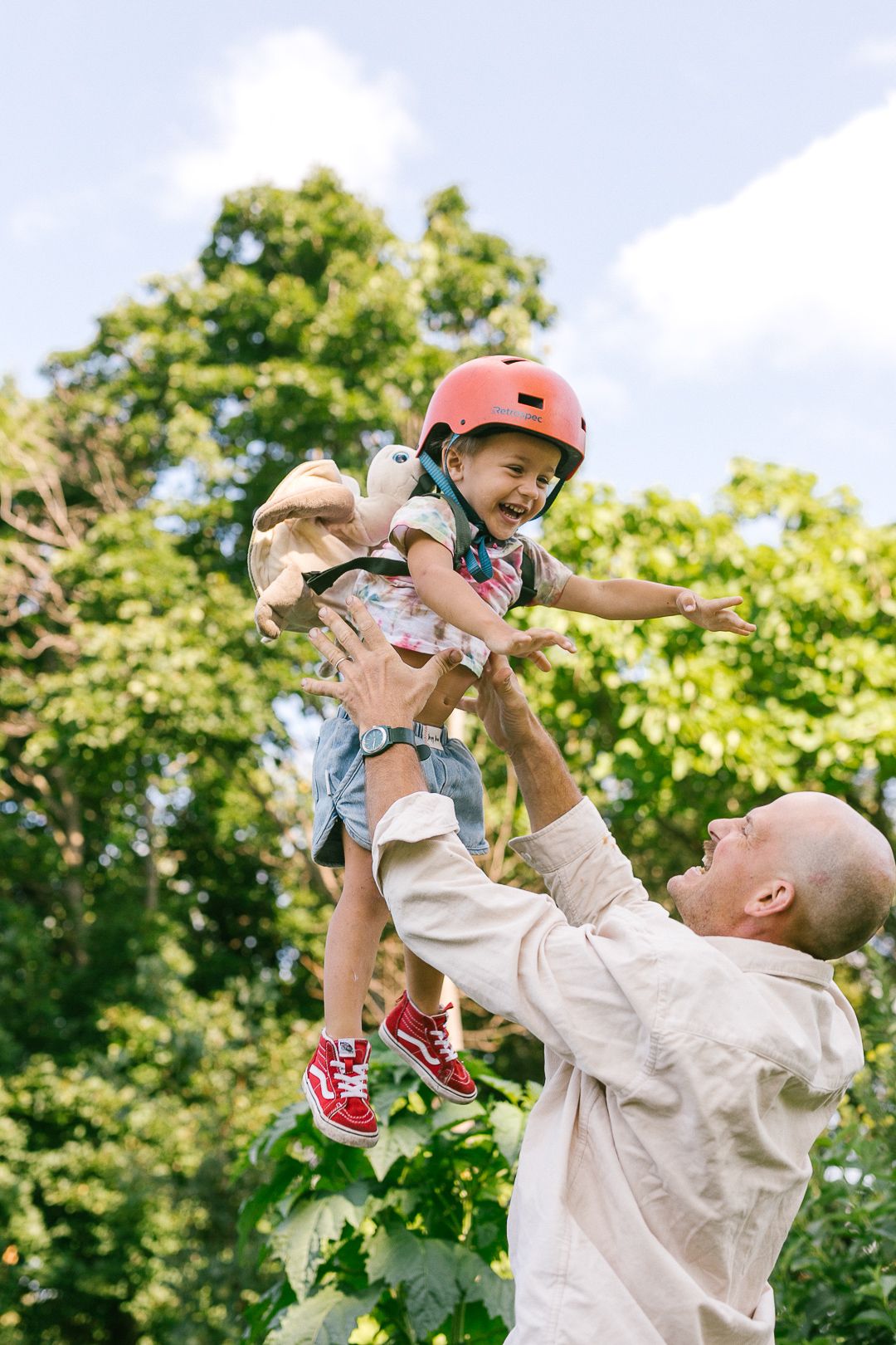 A child wearing a red helmet is lifted high into the air during outdoor play.