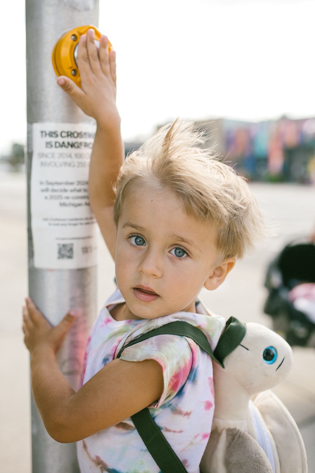 Young child in floral outfit reaching up towards yellow objects in bright sunlight.