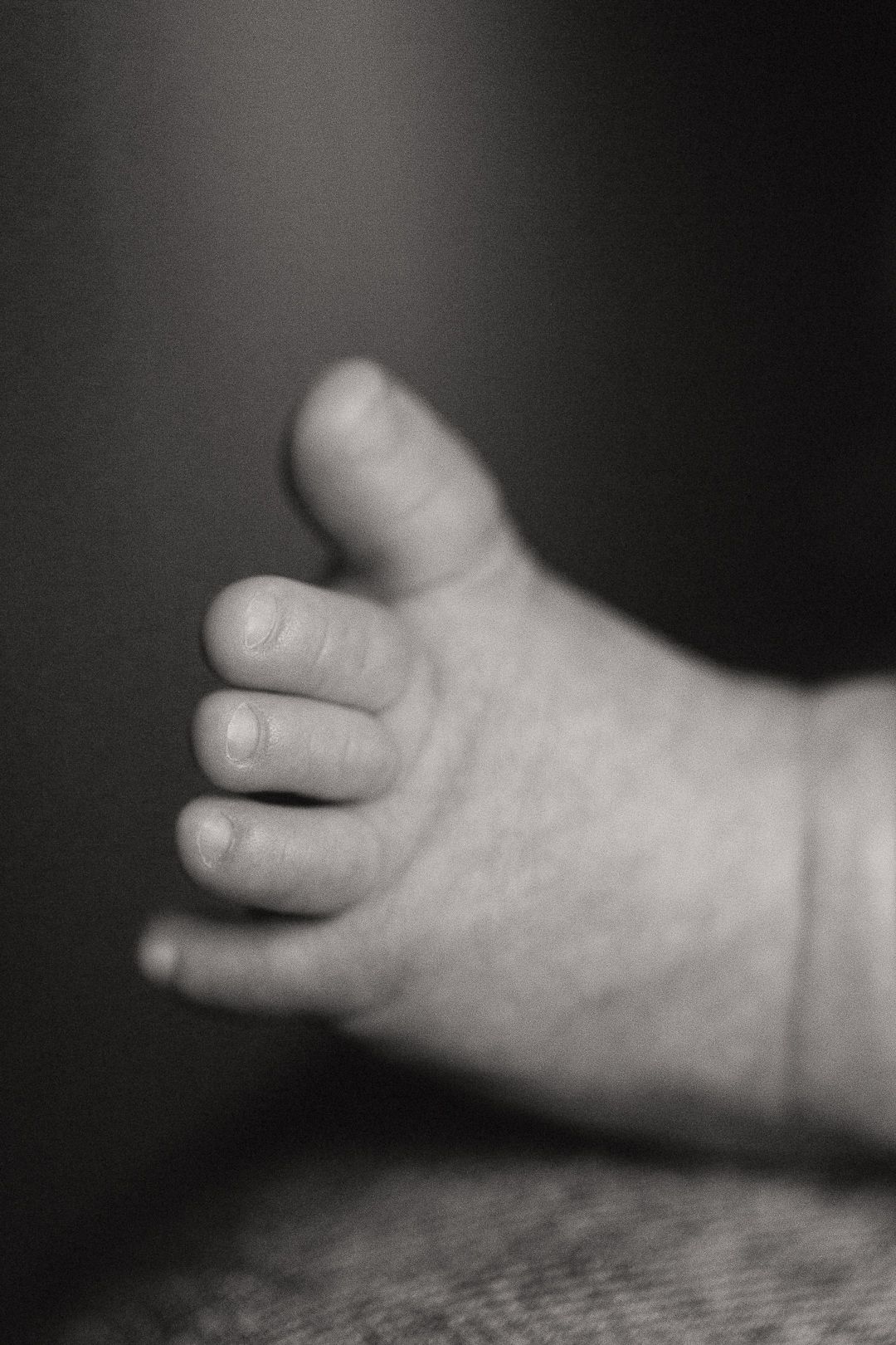 Close-up black and white photo of a small child's hand against a dark background.