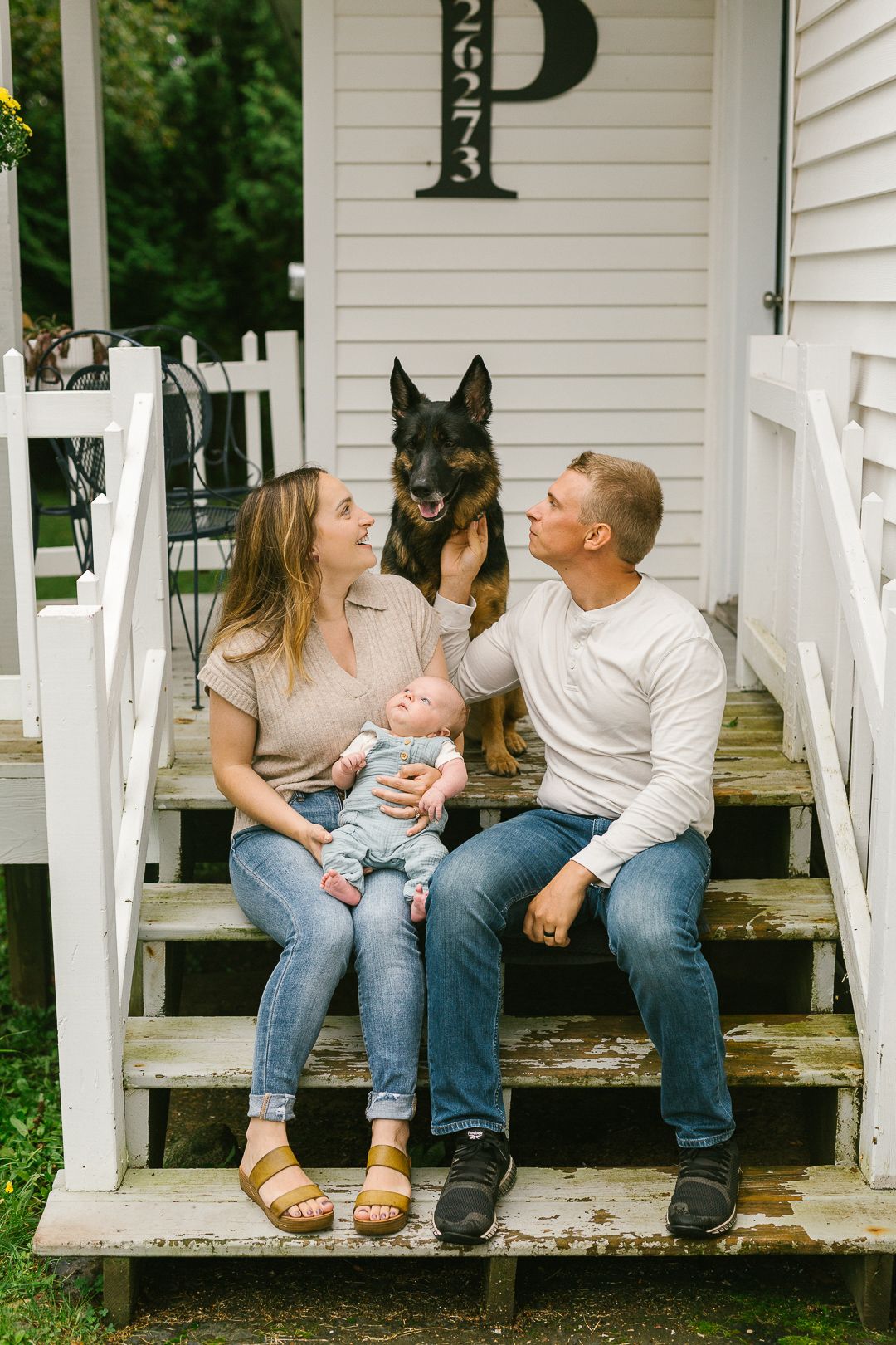 A family sits together on white porch steps with their dog on a sunny day.