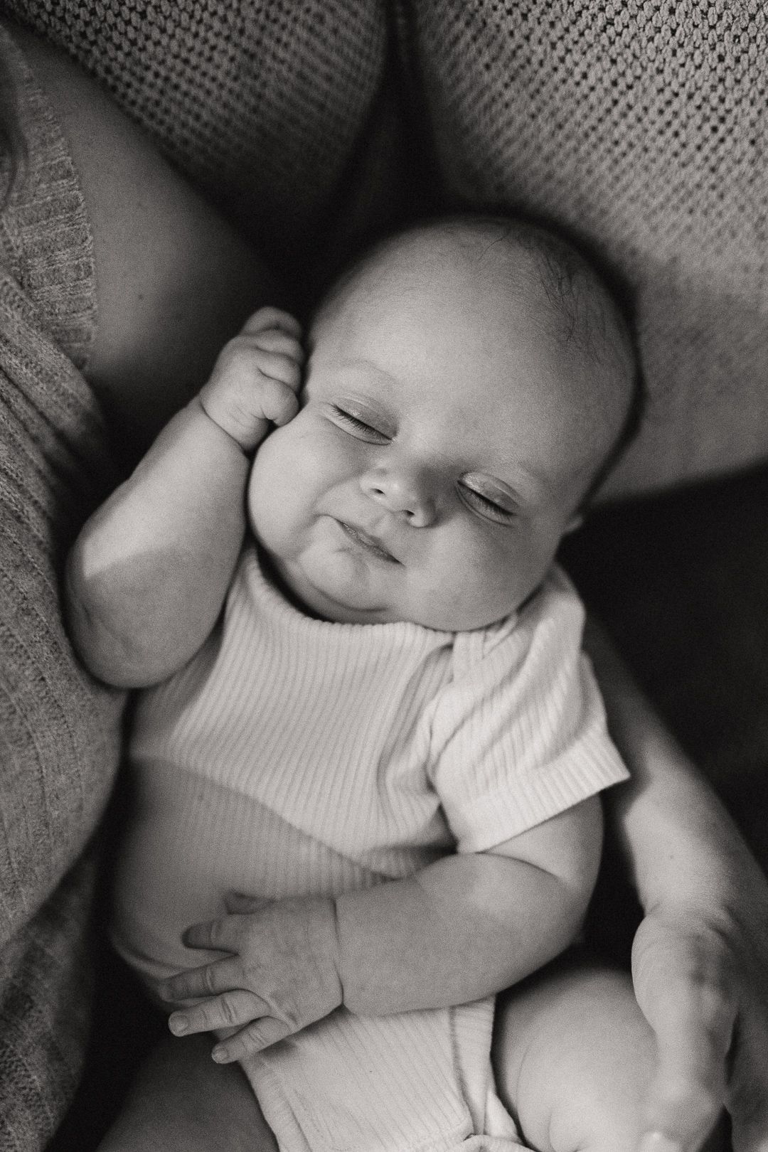 Peaceful sleeping newborn in black and white wearing soft white clothing against textured blanket.