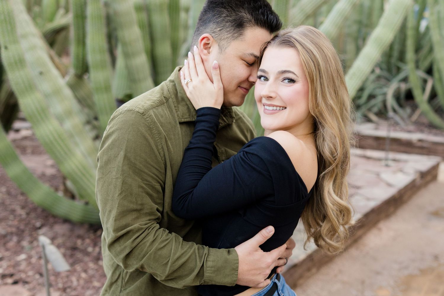 A couple embraces tenderly among desert cacti during an engagement photoshoot.