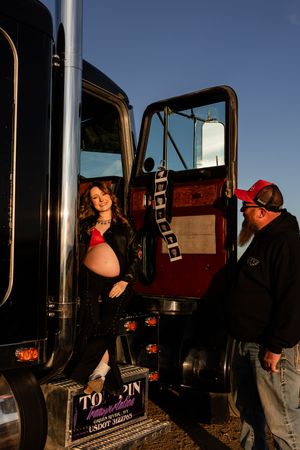 Truck drivers gather near their semi trucks during sunset, casting long shadows against the vehicles.