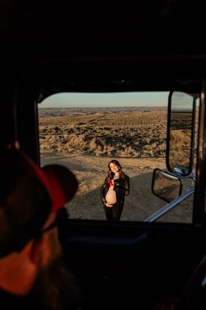 Desert landscape viewed through vehicle windows at sunset with silhouetted figures.