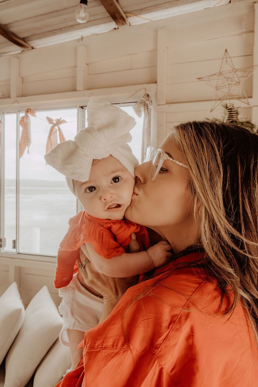 Person in red shirt playfully interacting with her new baby in a sunlit room at a central coast christmas photoshoot.