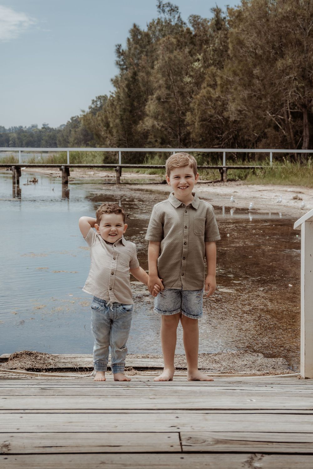 Two children pose together on a wooden dock by the water.