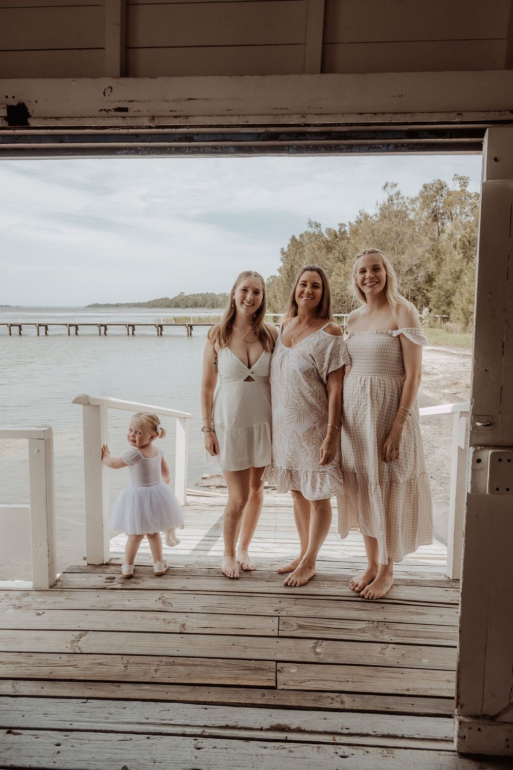 A row of light-colored dresses and bare feet line up along a waterfront deck.