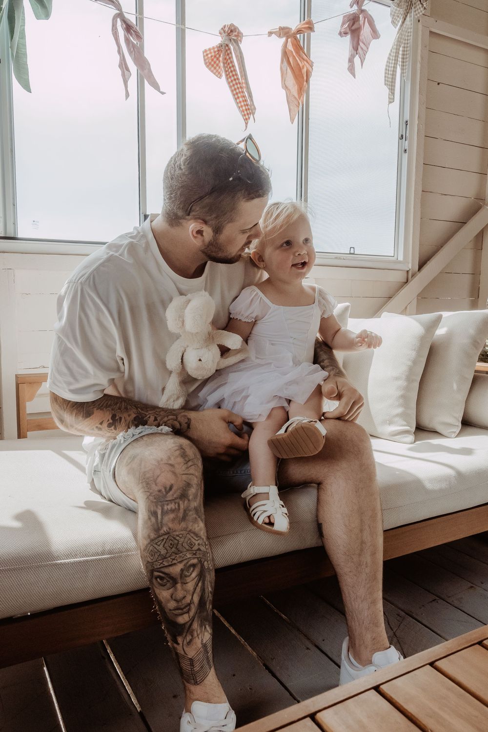 A tender moment shared between parent and child on a white couch by a window with decorations at a central coast christmas photoshoot.