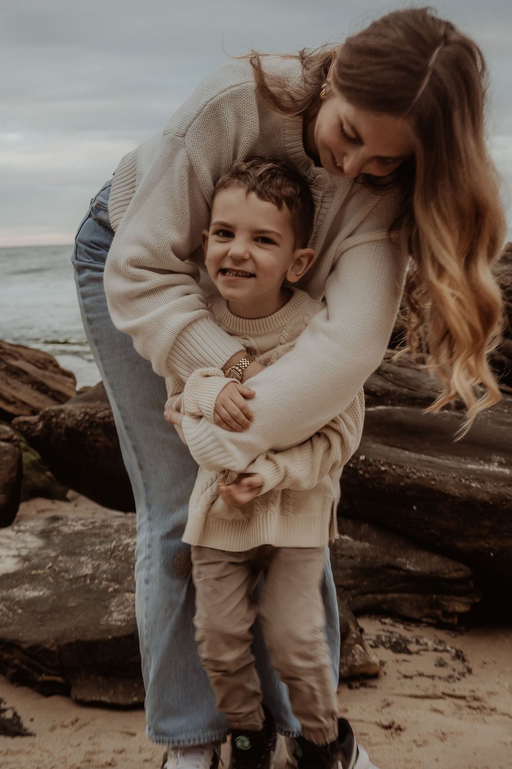 A tender embrace shared between parent and child on a rocky beach during a central coast family photoshoot.