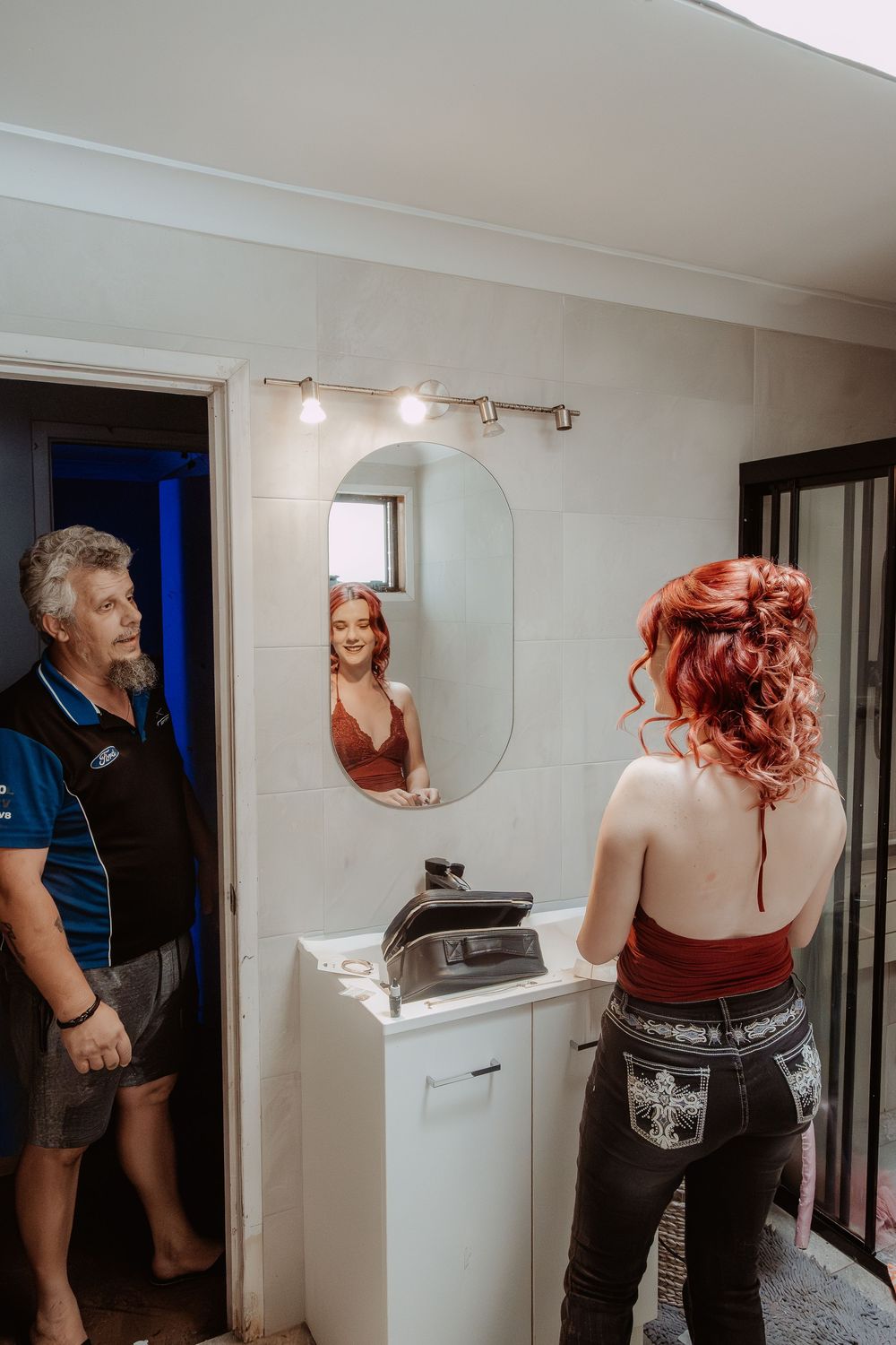 Getting ready sequence showing person with vibrant red hair preparing in bathroom mirror.
