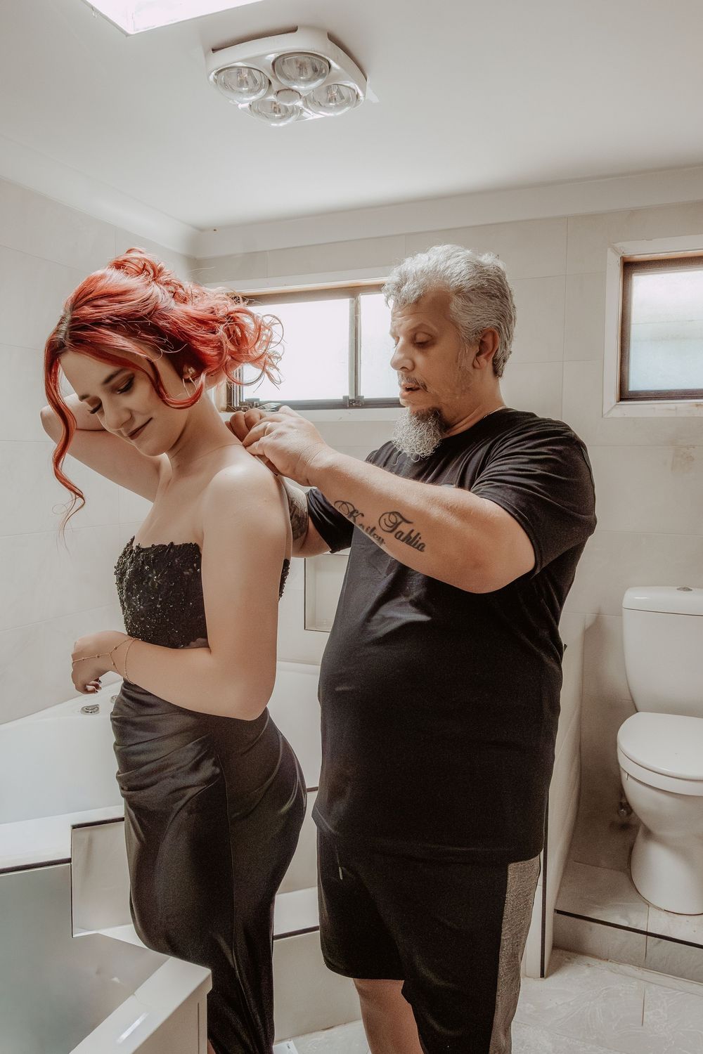Hair styling session in progress with stylist working on bright red hair in bathroom setting.