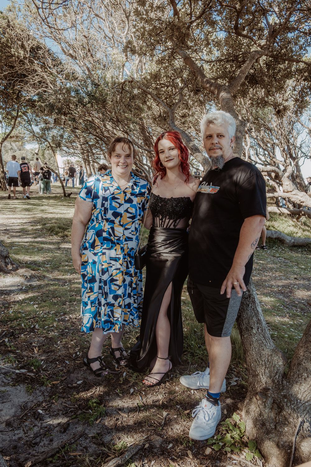 Family group photo under trees with person in black formal dress and others in casual attire.