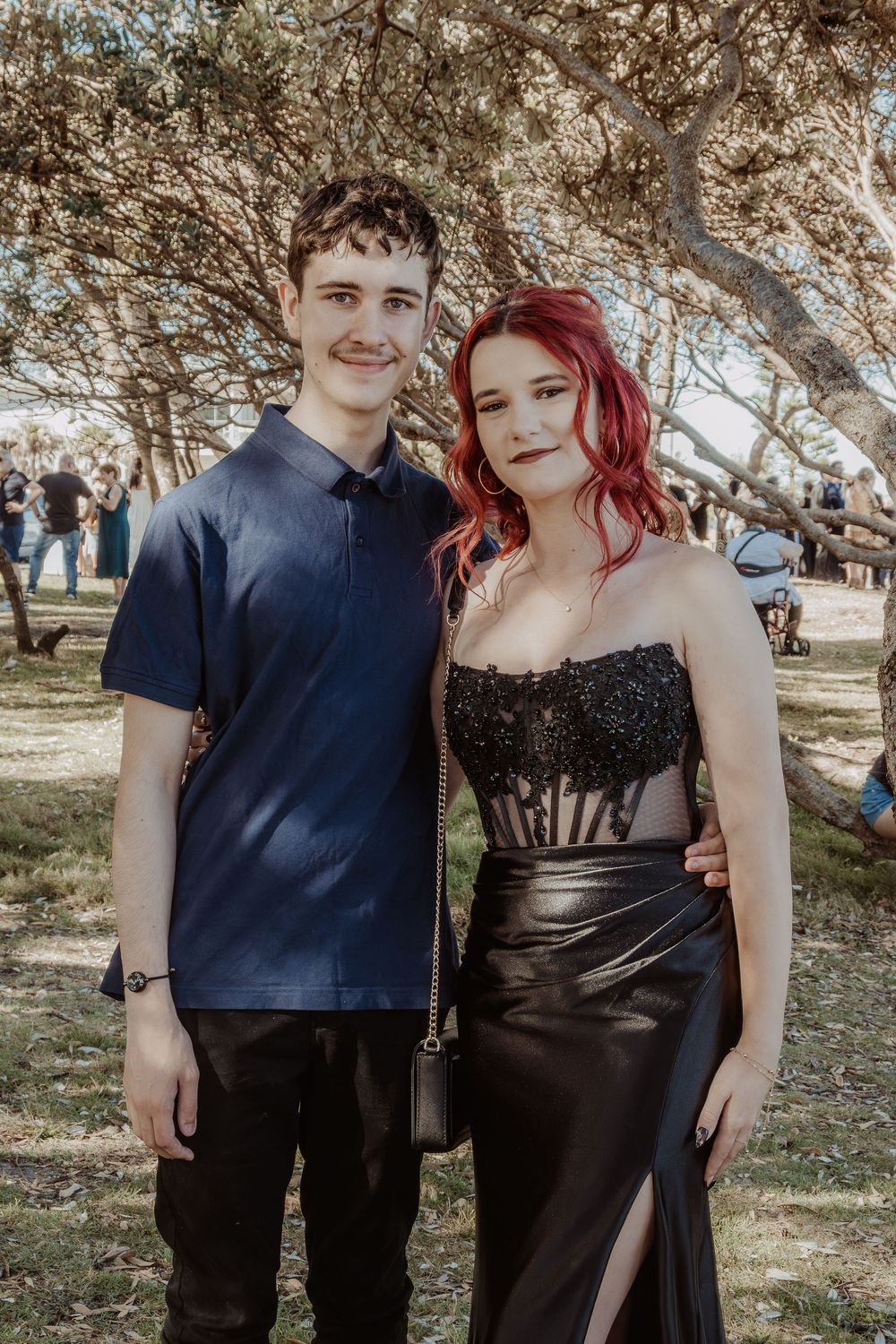 Formal portrait in outdoor park setting featuring black dress and styled red hair.