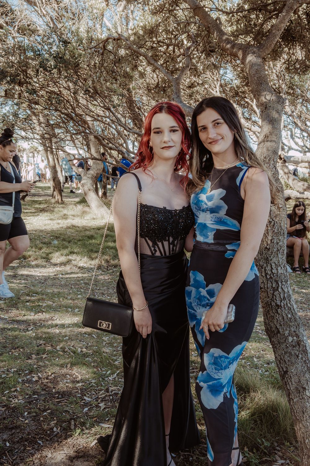 Two people in formal attire pose together in a wooded outdoor setting.