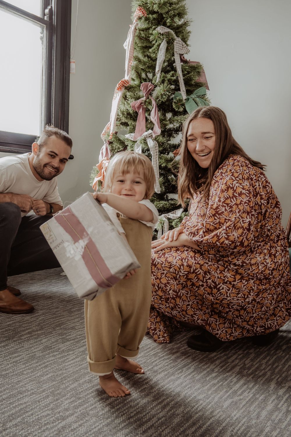 Family sits together opening Christmas presents in front of decorated tree on carpeted floor at a hunter valley christmas photoshoot.