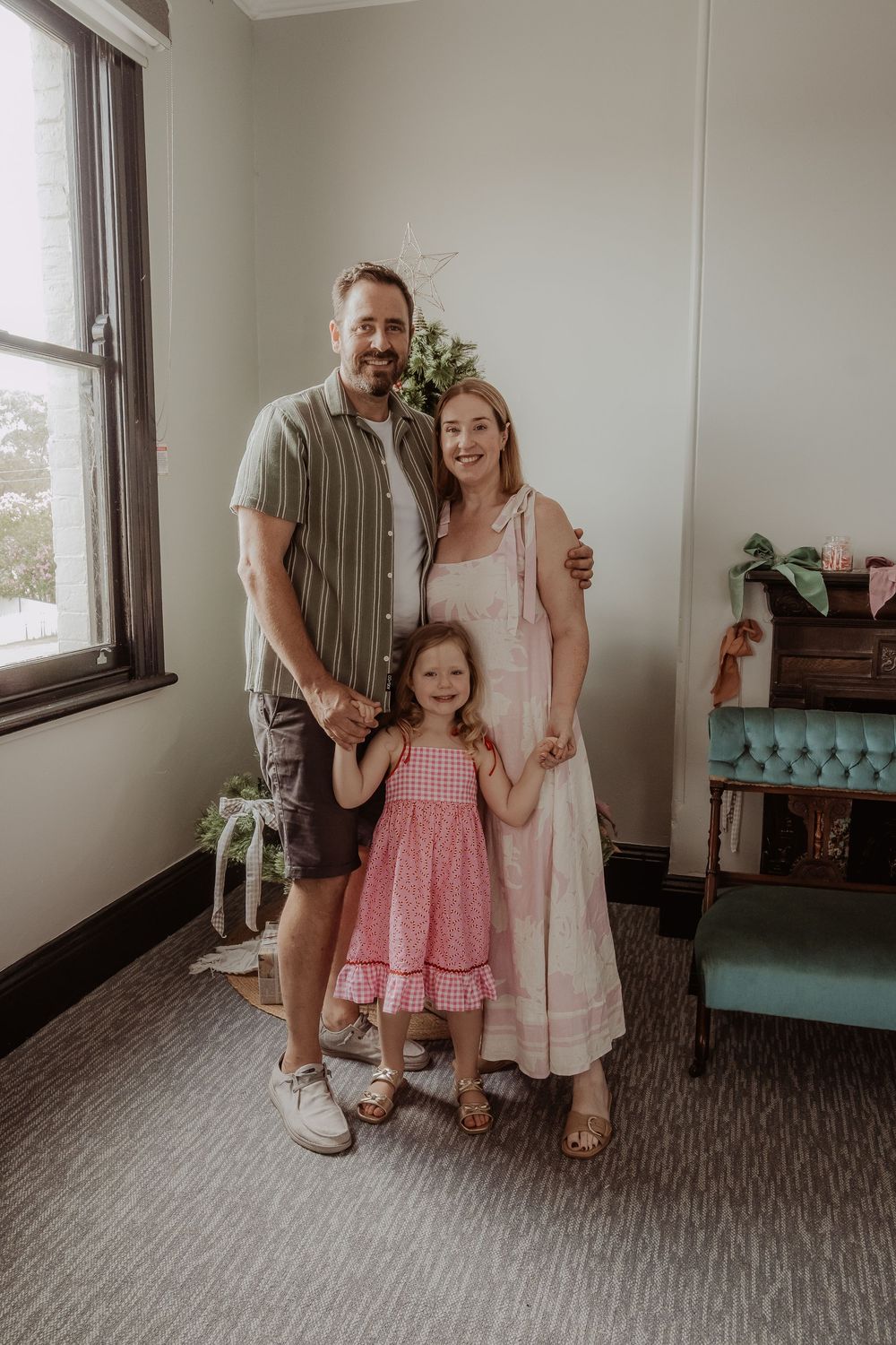 A family stands together in a room with gray carpeting and white walls at a hunter valley christmas photoshoot.