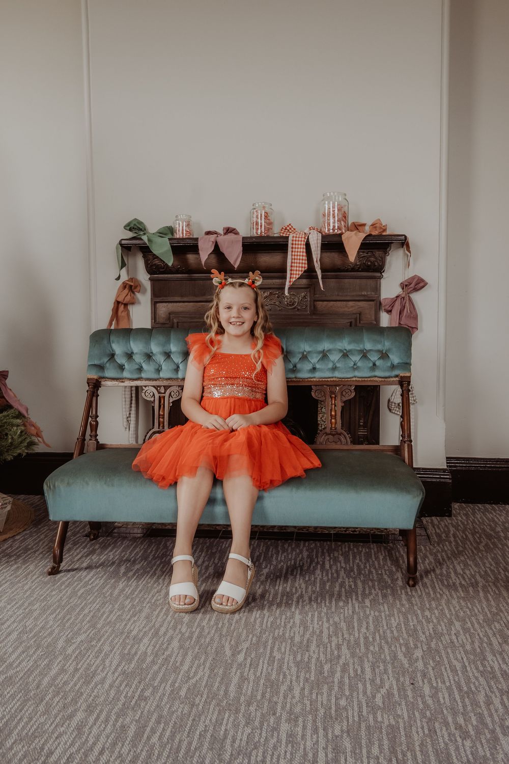 A child in a red dress sitting on a teal vintage bench against a white wall at a hunter valley christmas photoshoot.