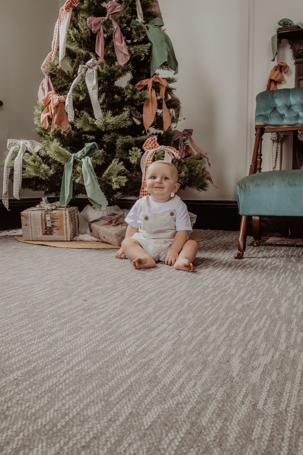 Baby sitting on carpet in front of decorated Christmas tree with pink bows at a hunter valley christmas photoshoot.