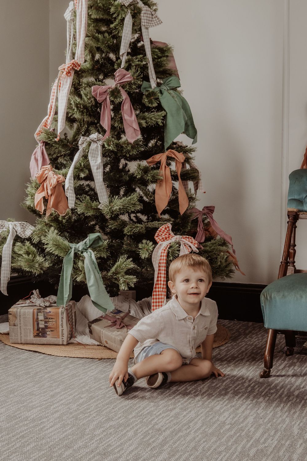 A small child crawls on carpeted floor near a decorated Christmas tree with ribbons at a hunter valley christmas photoshoot.