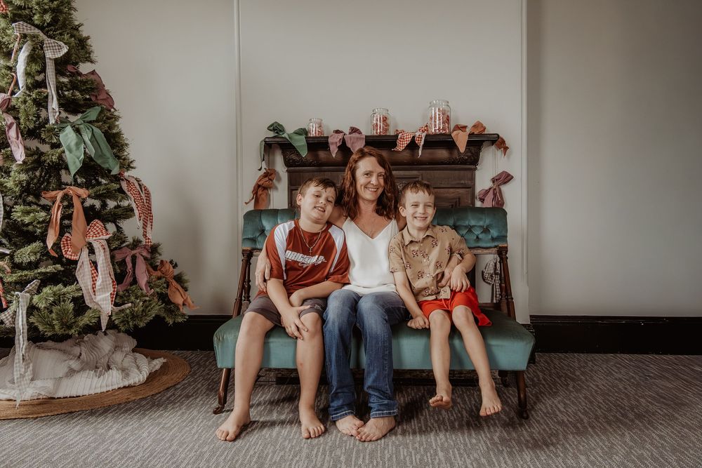 Family sitting together on a teal vintage bench with Christmas tree in cozy living room setting at a hunter valley christmas photoshoot.