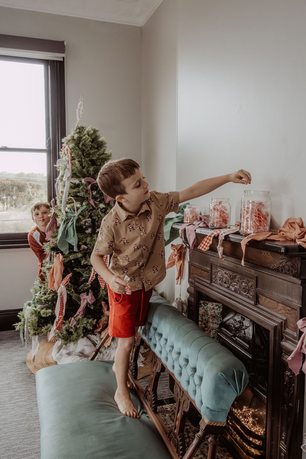 Children playing and reaching for decorations near a Christmas tree in a cozy home setting at a hunter valley christmas photoshoot.