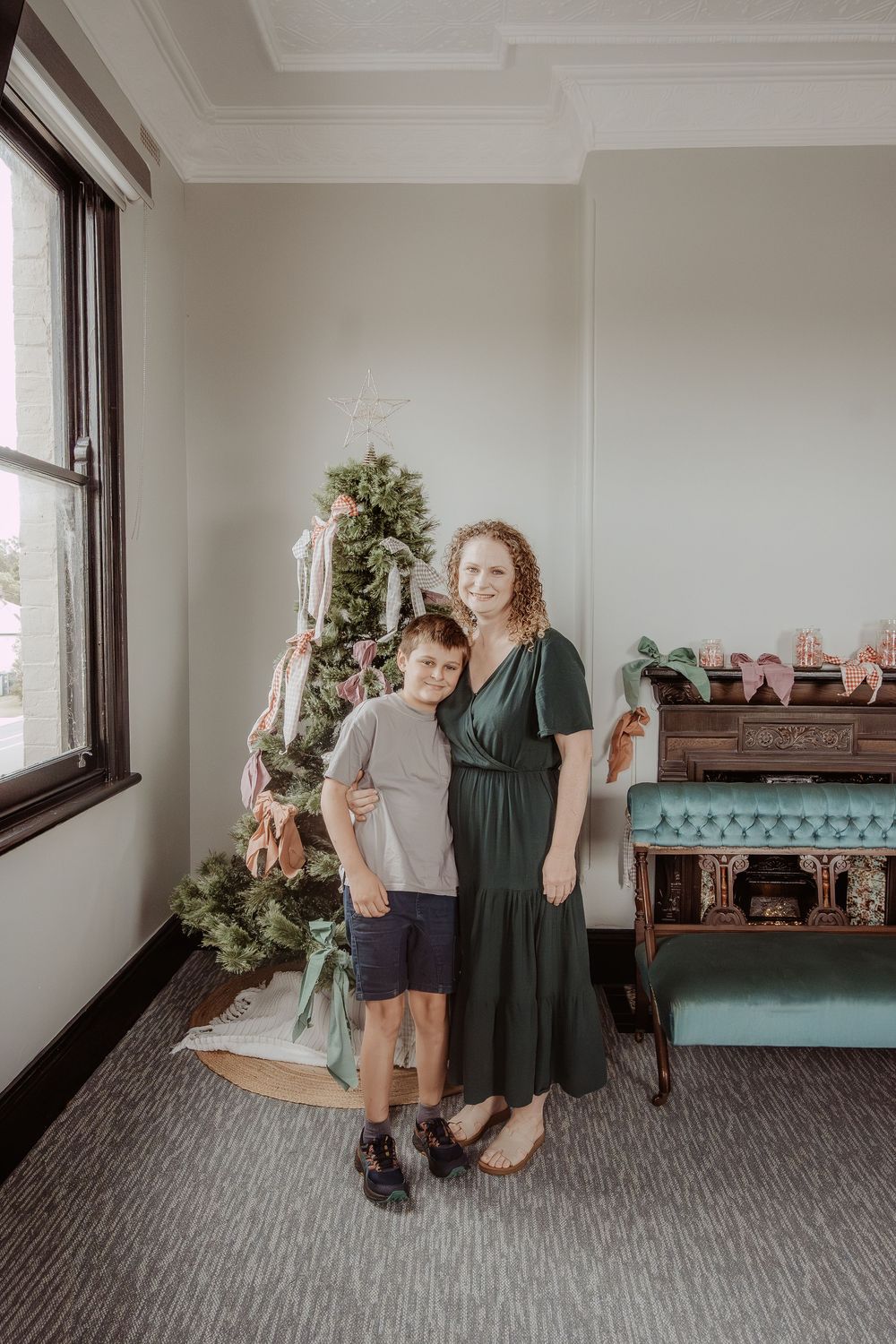 A festive scene with a Christmas tree, vintage furniture and two people standing next to eachother at a hunter valley christmas photoshoot.