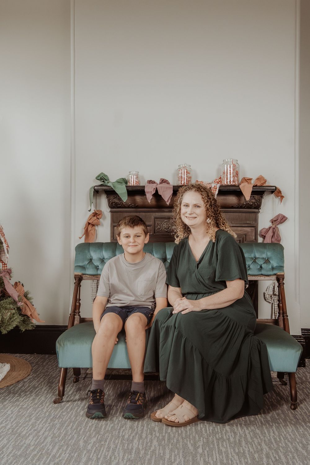 Mother and son sitting together on a teal blue couch in an indoor christmas themed setting at a hunter valley christmas photoshoot.