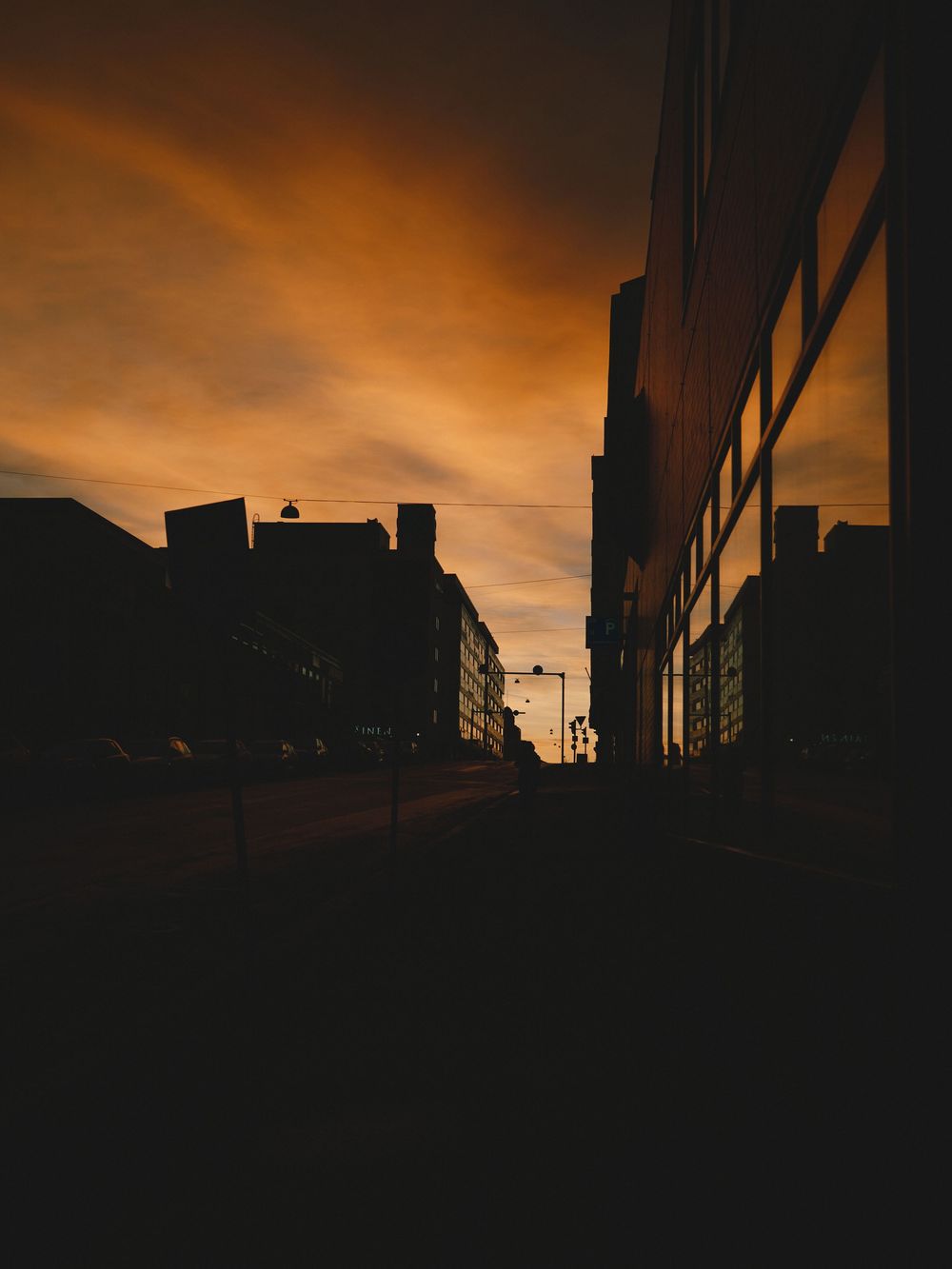 Dark urban silhouettes of buildings against a dramatic orange and black sunset sky create a moody cityscape view.