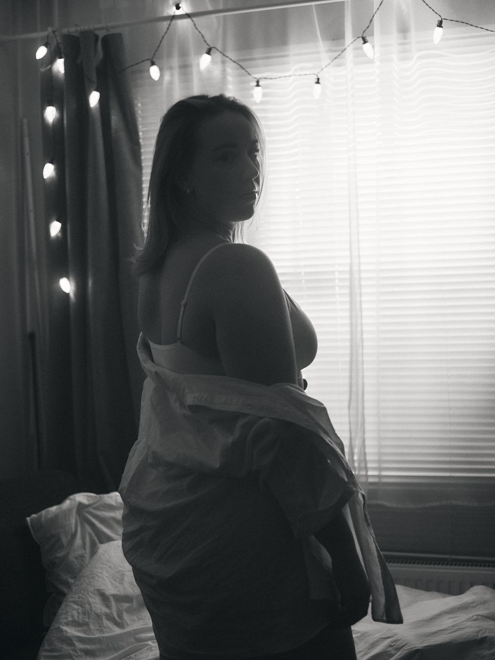 Moody black and white silhouette by window with string lights creating an intimate boudoir atmosphere.