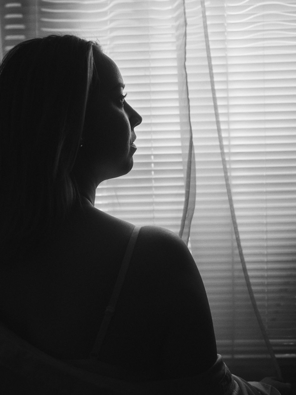 Dramatic black and white profile silhouette against window blinds in soft natural lighting.