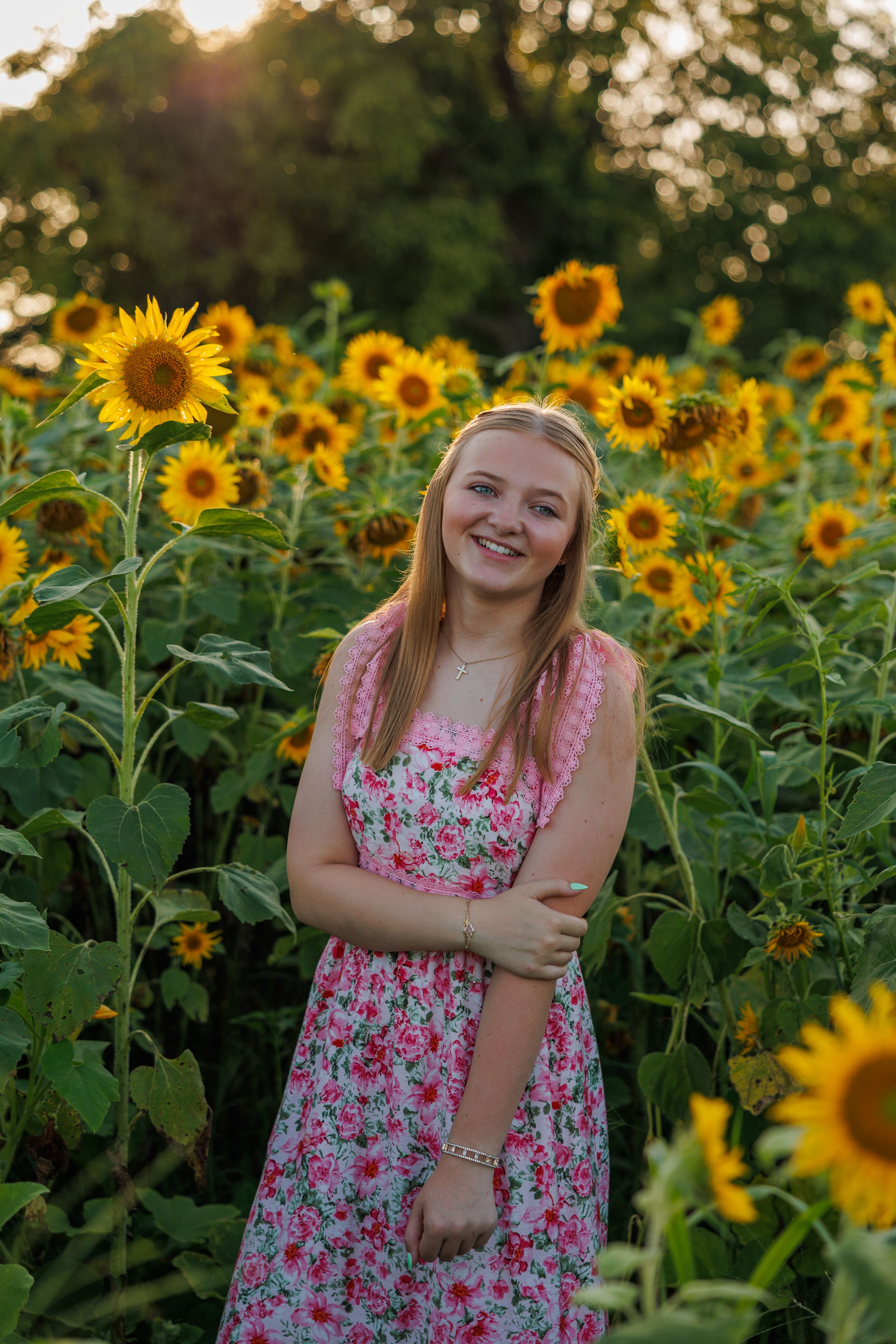 A beautiful sunflower field at sunset with someone in a pink floral dress enjoying nature.