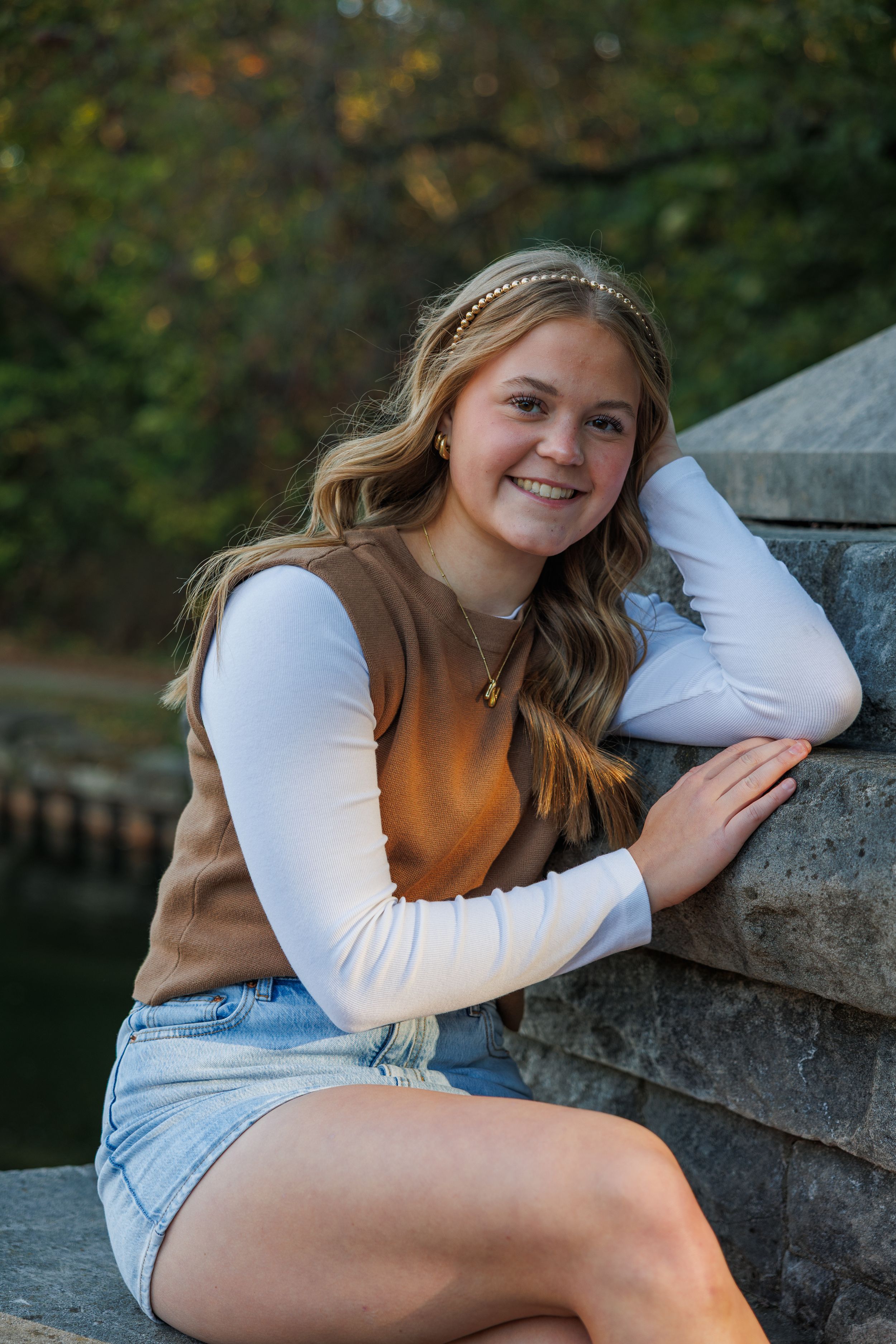A person in a brown vest and white long sleeve shirt sits casually on stone steps outdoors.