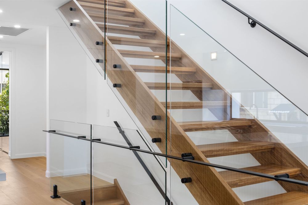 Modern wooden staircase with glass balustrade in a bright white interior.