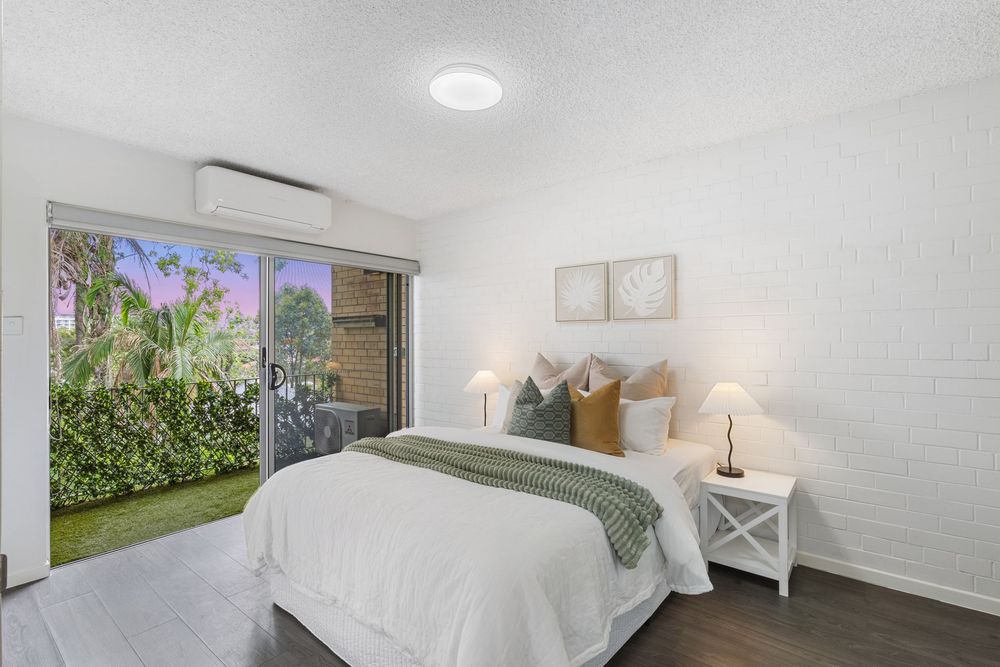 Bright bedroom with white bedding, minimalist decor, and natural light streaming through windows.