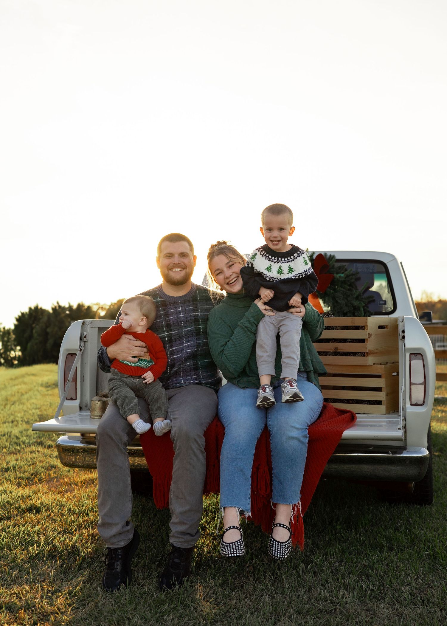 Family enjoying a festive Texas farm Christmas mini session, sitting on the bed of an old red Ford truck decorated with holiday greenery.