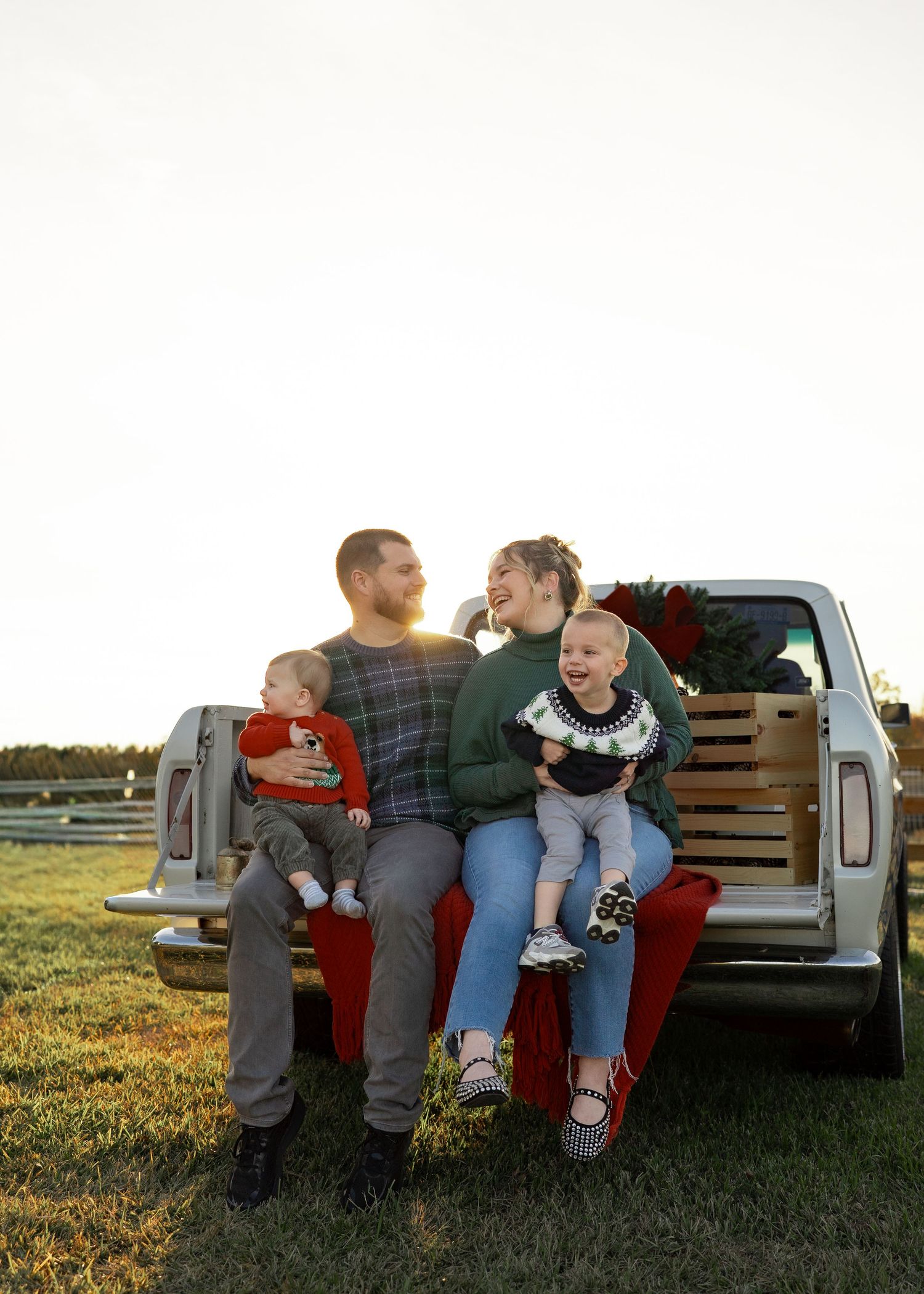 Family enjoying a festive Texas farm Christmas mini session, sitting on the bed of an old red Ford truck decorated with holiday greenery.