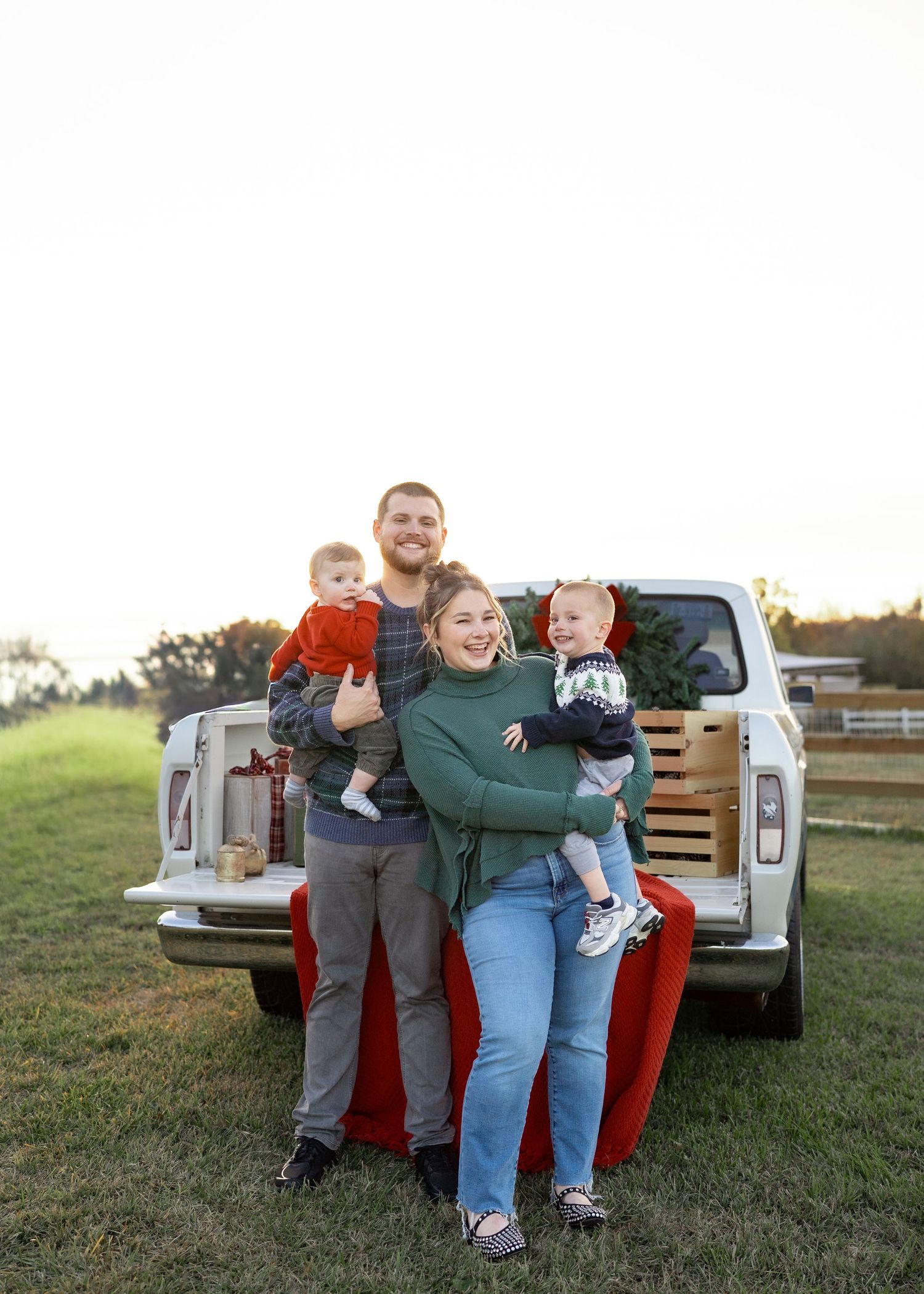 Family enjoying a festive Texas farm Christmas mini session, sitting on the bed of an old red Ford truck decorated with holiday greenery.