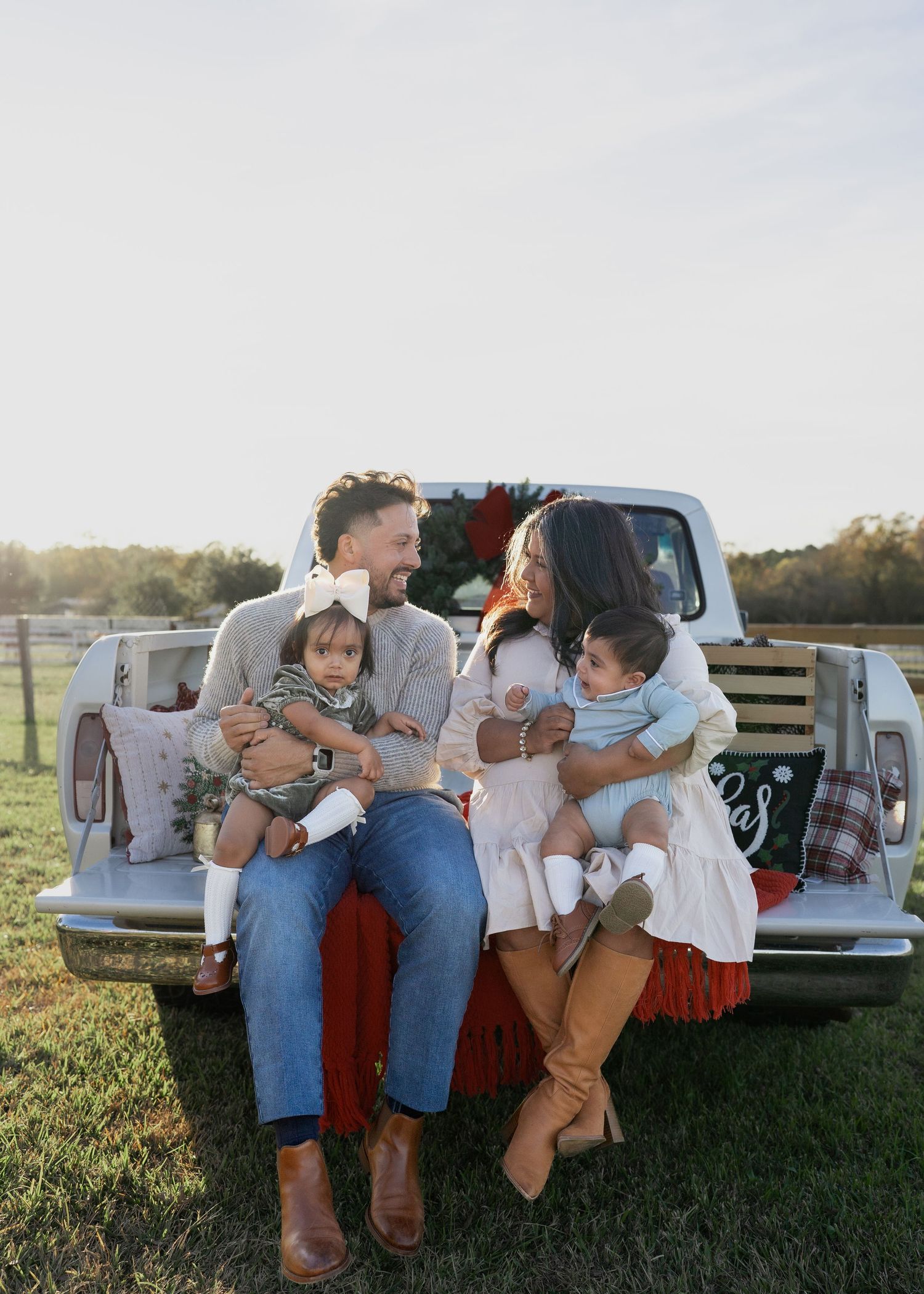 Family enjoying a festive Texas farm Christmas mini session, sitting on the bed of an old red Ford truck decorated with holiday greenery.