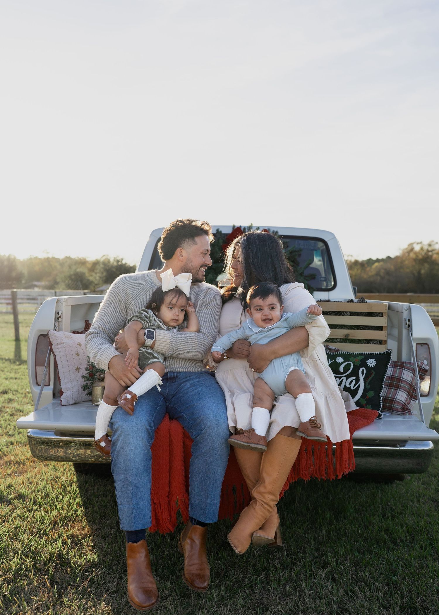 Family enjoying a festive Texas farm Christmas mini session, sitting on the bed of an old red Ford truck decorated with holiday greenery.