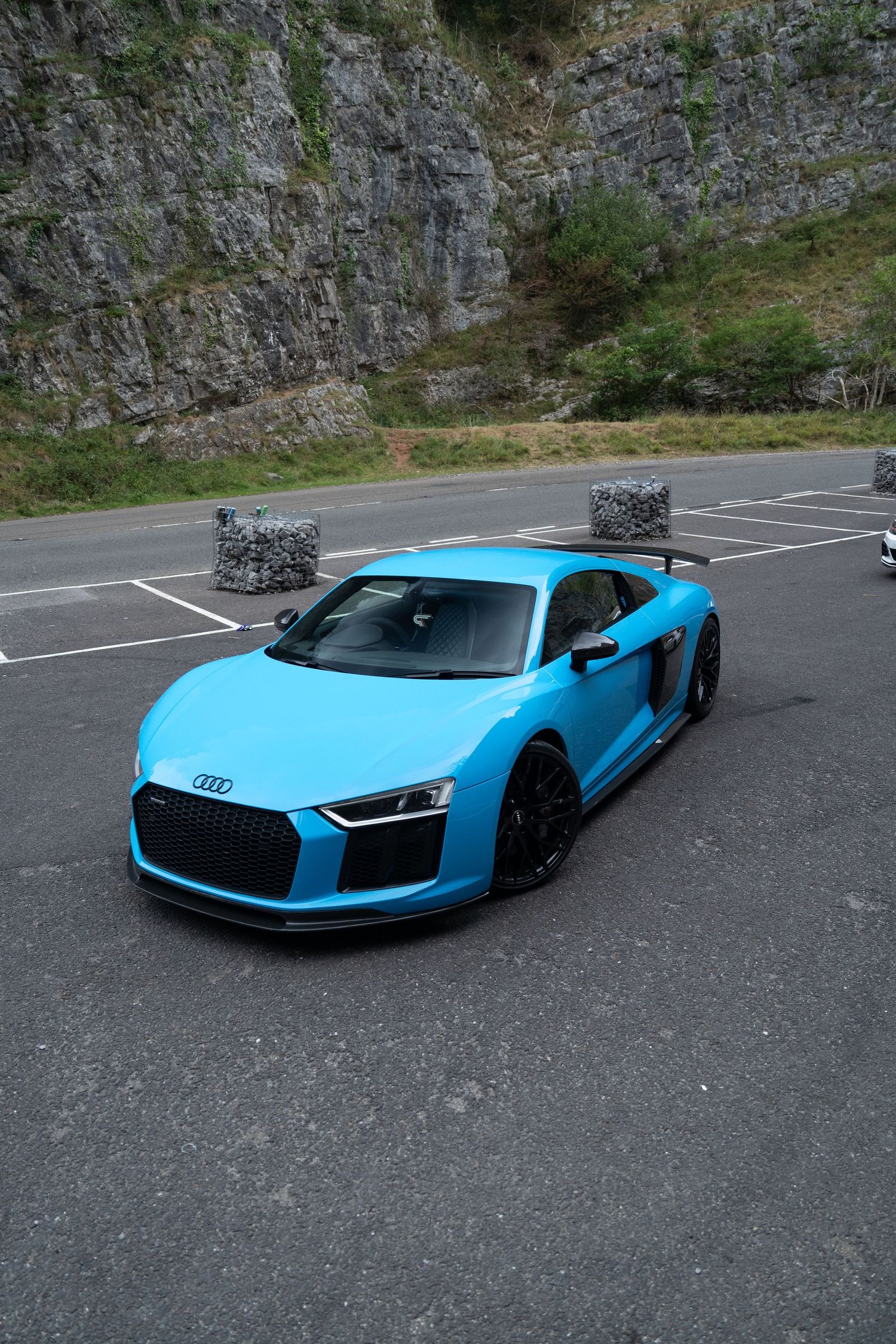 Bright blue Audi R8 supercar parked in front of a rocky cliff face.